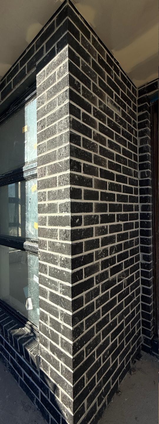 Black brick window return before cleaning, with mortar splash and construction dust on the face