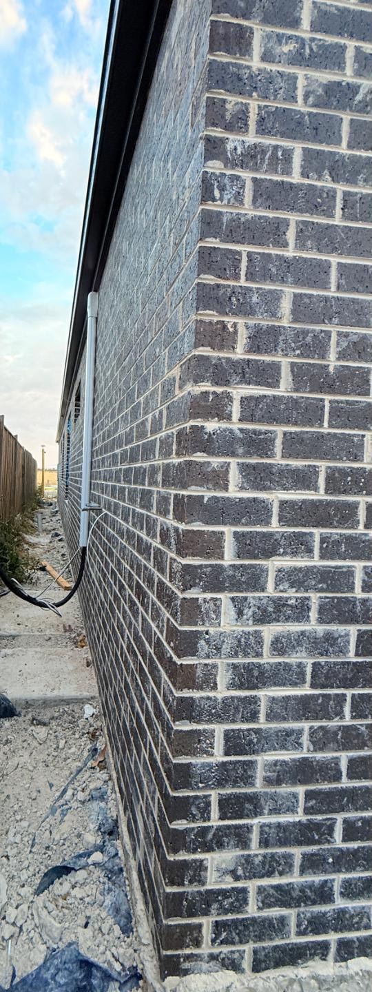 New build charcoal brick corner before cleaning, with heavy grey mortar haze across the brickwork