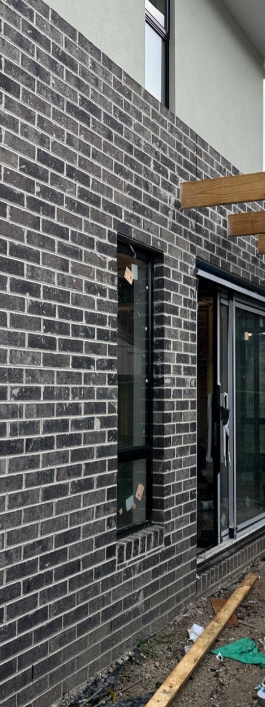 Dark brick elevation before cleaning, with grey cement film dulling the brickwork around the windows