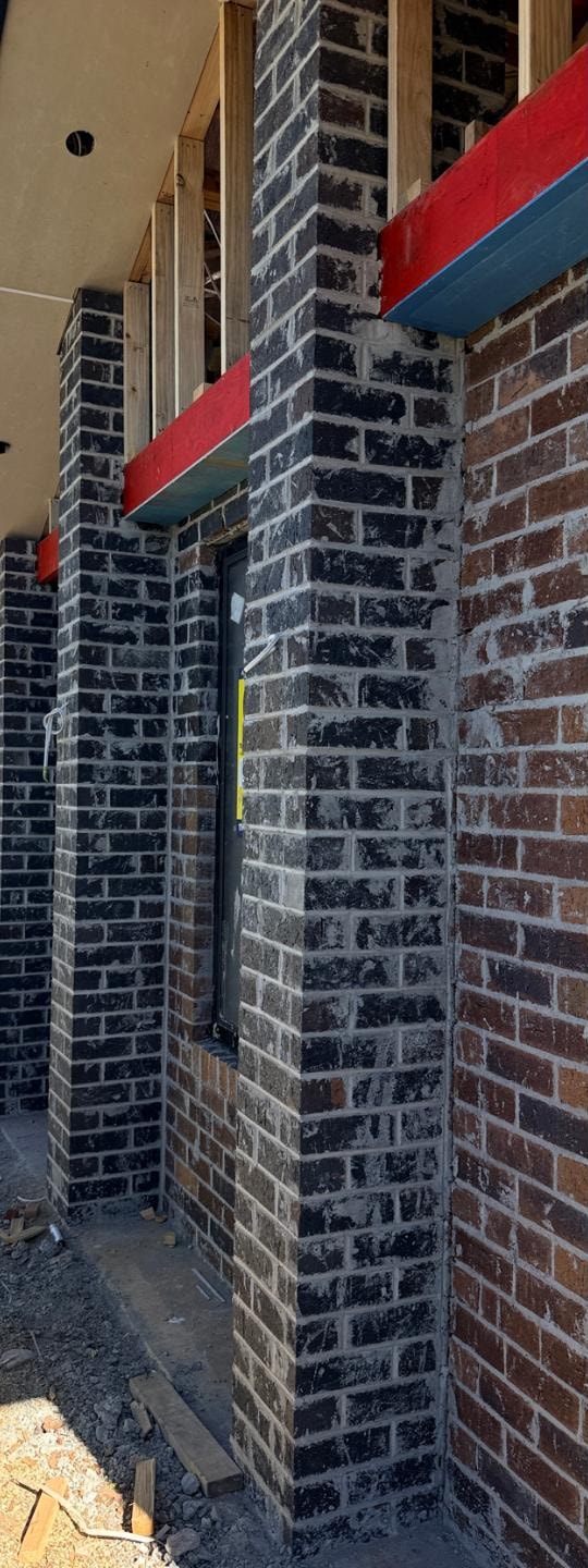 Brick entry piers before cleaning, with mortar smear across the face, mid-construction