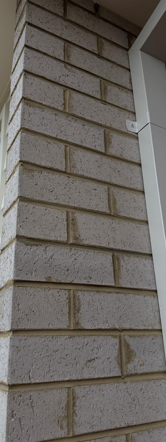 Grey brick pier before cleaning, with mortar dragged down the face of the brickwork